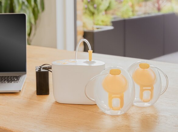 Pump In Style® Hands-free double electric breast pump Medela Pump In Style® Hands-free double electric breast pump sitting on office desk with the pump, Hands-free collection cups and battery pack charger