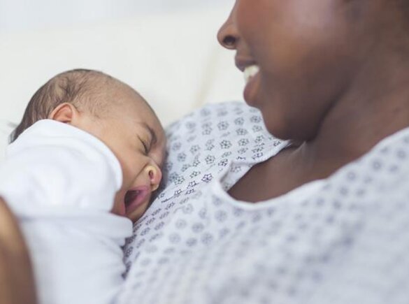 A smiling mom sits in a hospital with her newborn baby on her chest.