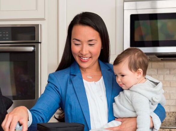 A mom getting ready to go to work while holding her baby on her hip in the kitchen.