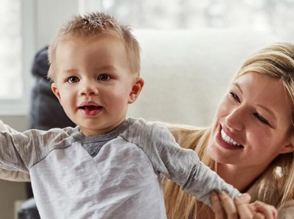 A smiling mom helps a boy learn to stand, then walk.