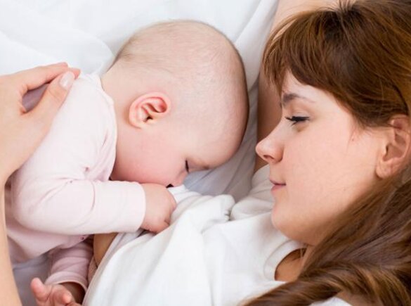 A mom watches as her baby sleeps in the bed next to her.