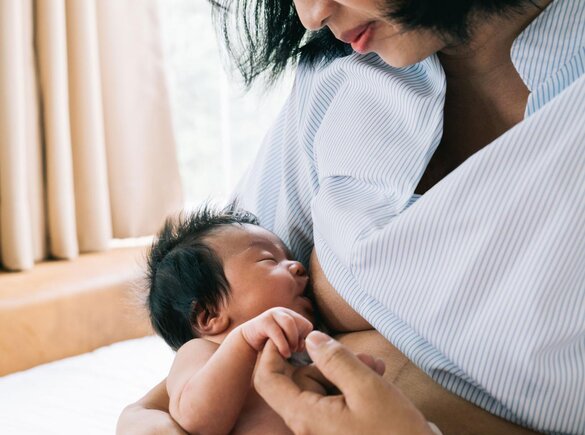 A baby holds its mother's finger while breastfeeding.