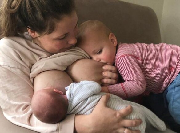 Two babies are breastfed in tandem by their mother.