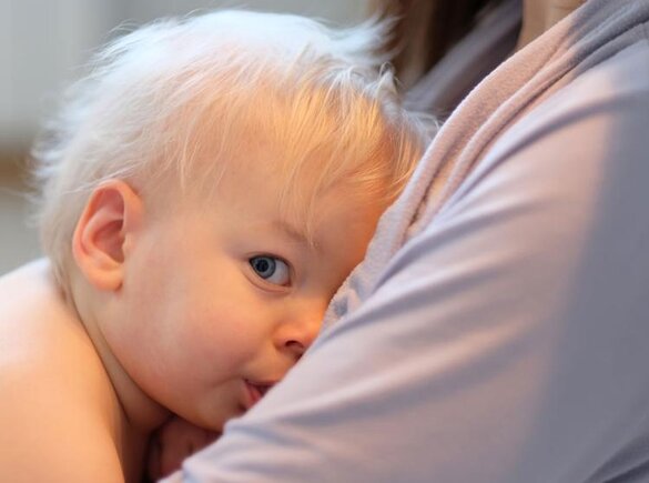 A child breastfeeds while sitting on his mother's lap.