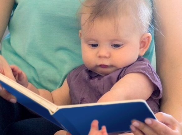 A mom and her baby read a book.