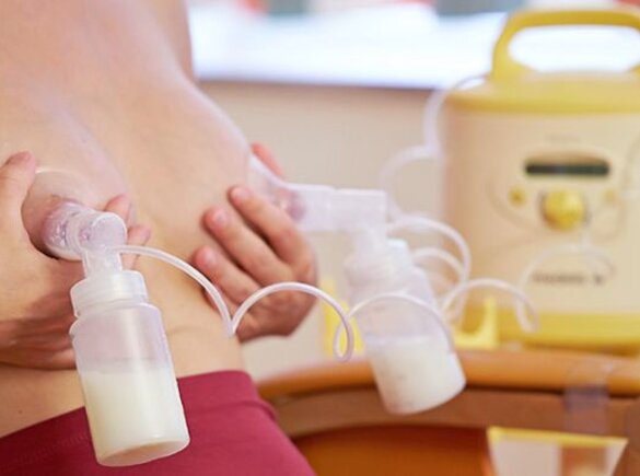 Woman sitting in a chair double pumping using a Medela Symphony breast pump.