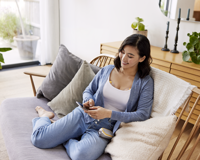 Mom sitting on couch using her phone while pumping with her Medela Freestyle™ Hands-free double electric wearable breast pump