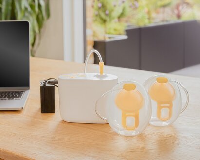 Medela Pump In Style® Hands-free double electric breast pump sitting on office desk with the pump, Hands-free collection cups and battery pack charger