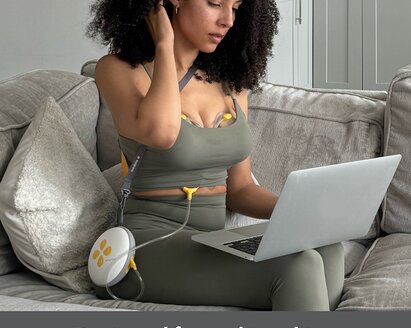 Woman sitting on counch using laptop while pumping with the Medela Swing Maxi™ double electric breast pump.  Text at bottom of image says, "Designed for multi-tasking"