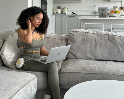 Mom wearing a Medela Swing Maxi™ double electric breast pump while sitting on her couch working from her laptop.