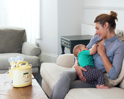 Mom on couch breastfeeding baby with Medela Symphony® breast pump on table in front of her ready to use