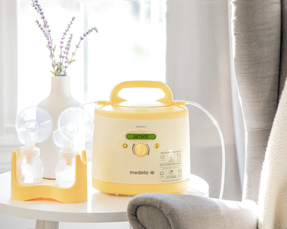 Tire-lait Medela Symphony PLUS® sur une table dans une pièce ensoleillée à côté d'une chaise