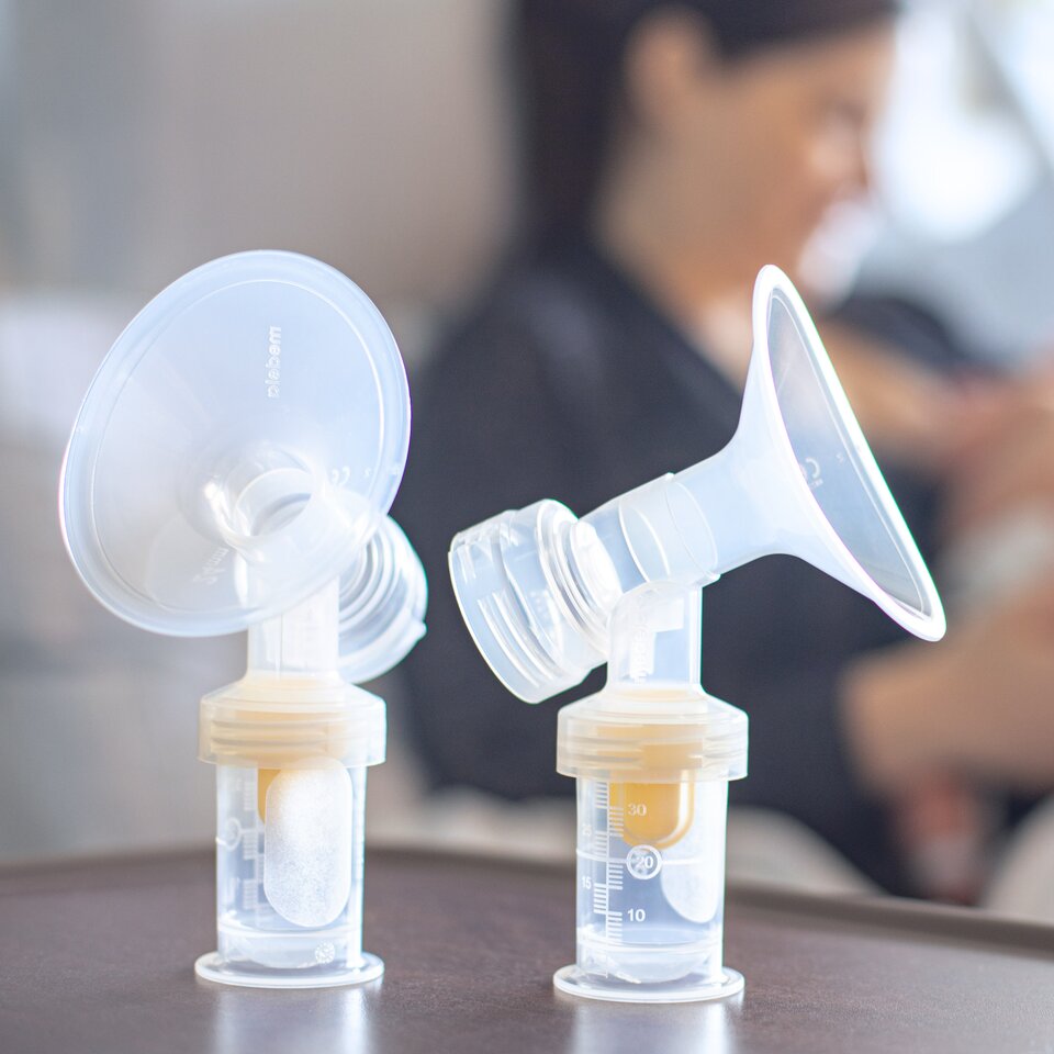 Mom feeding newborn in hospital bed with Medela PersonalFit™ PLUS breast shields in the foreground