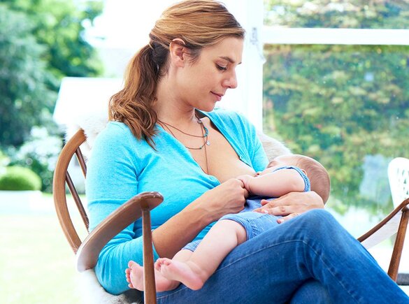 Power of Breastmilk A mom breastfeeds her baby while sitting in a rocking chair by the window.