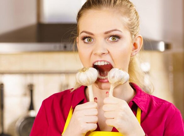 Eine Frau in einer Schürze hält Knoblauchzehen mit offenem Mund.