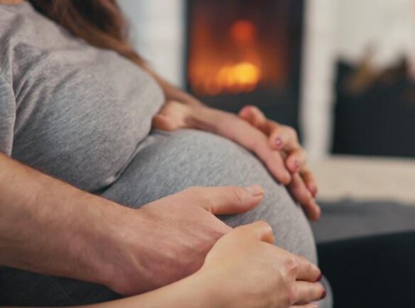 Woman sitting with her hands and her husbands hands on her pregnant belly.