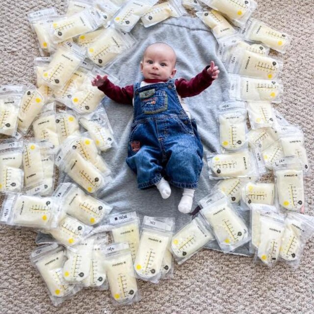 Baby laying on the ground surrounded by breast milk storage bags filled with breast milk.