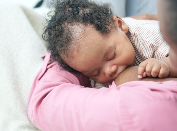 Breastfeeding Challenges A baby breastfeeding on its mom's lap while at home.