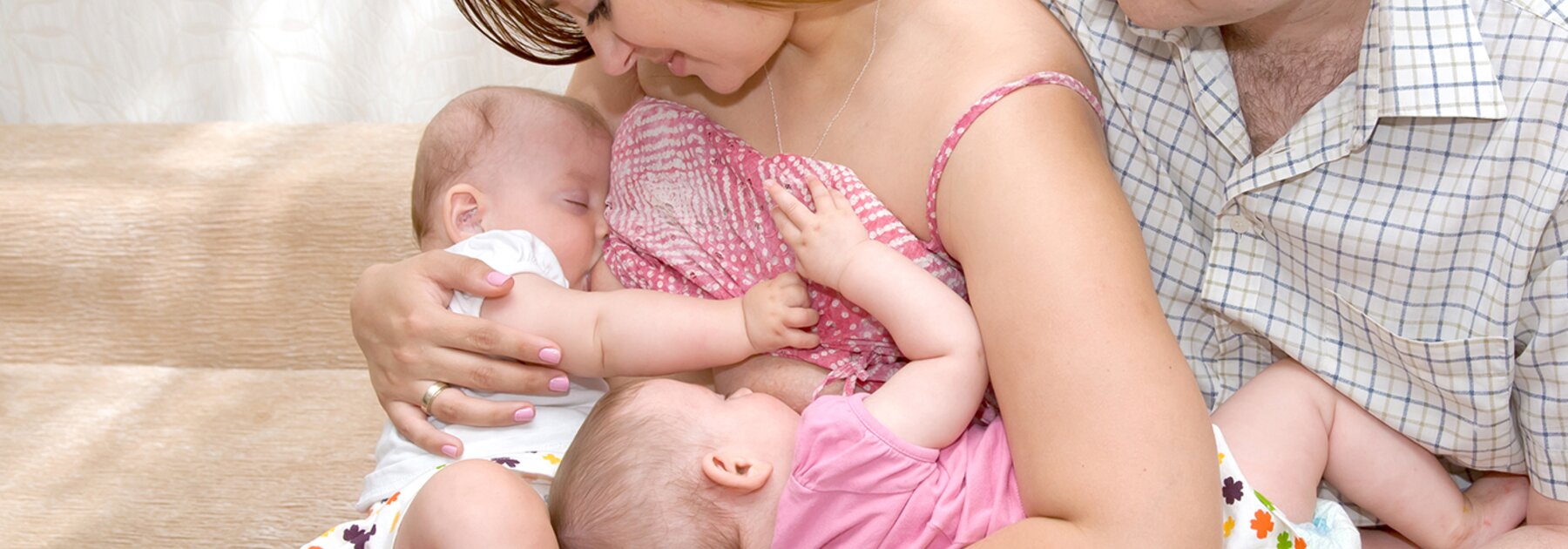 Breastfeeding Tips A mom feeds her twins in tandem while the dad sits next to them and supports one of the babies.