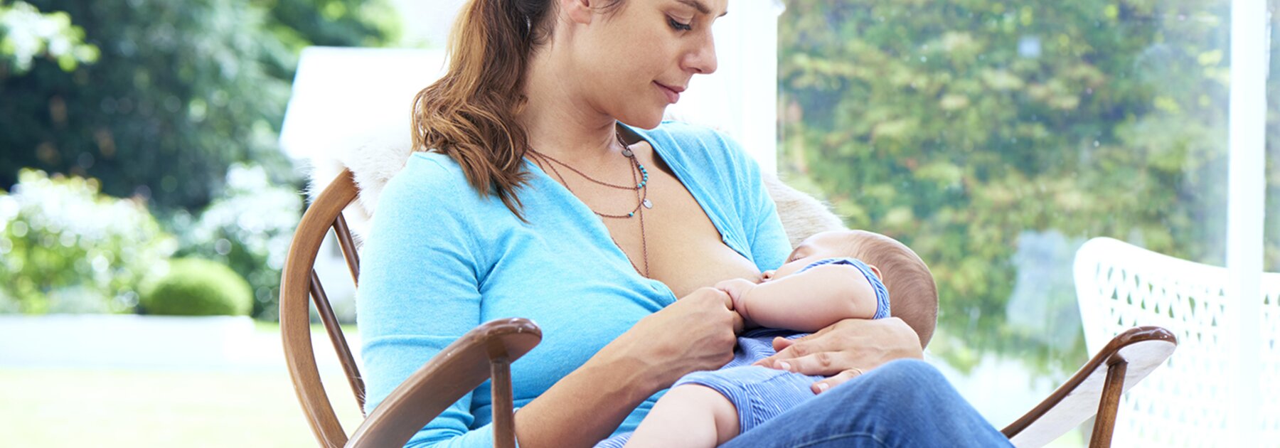 A mom breastfeeds her baby while sitting in a rocking chair by the window.