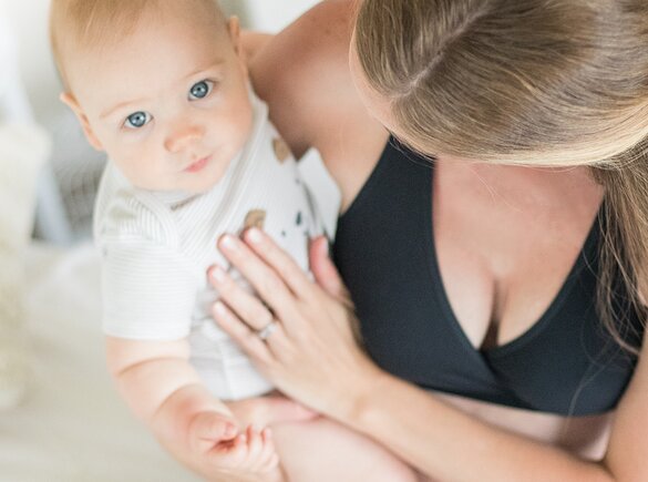 Breastfeeding Tips A baby looks into the camera above while being held by its mom.