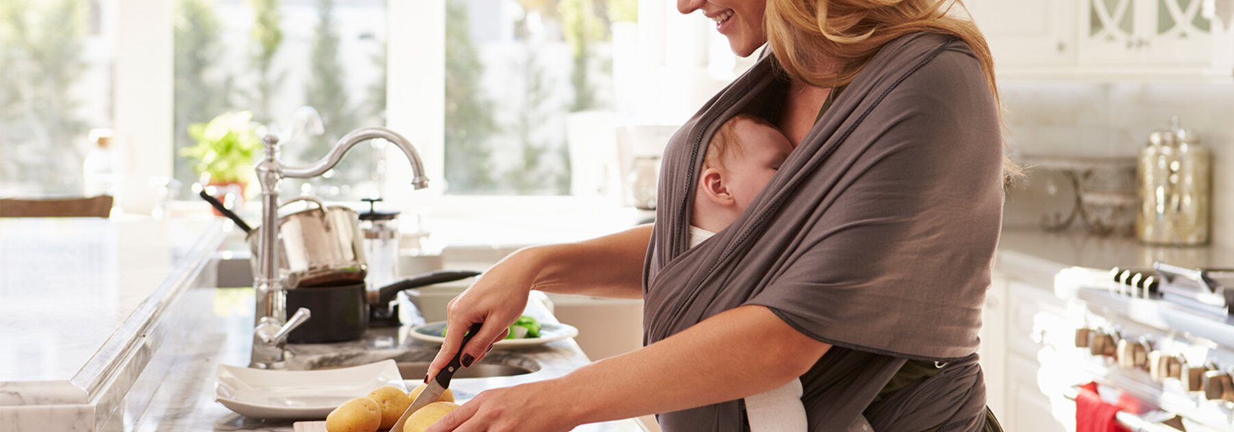 Breastfeeding Tips A mother prepares a healthy meal to support good nutrition during breastfeeding while her baby sleeps in a sling attached to her.