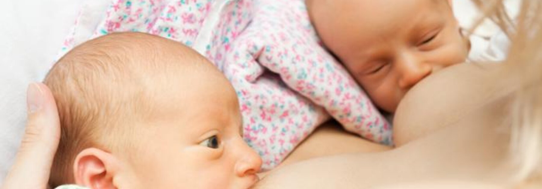 Mother breastfeeding twins in double rugby ball hold position.